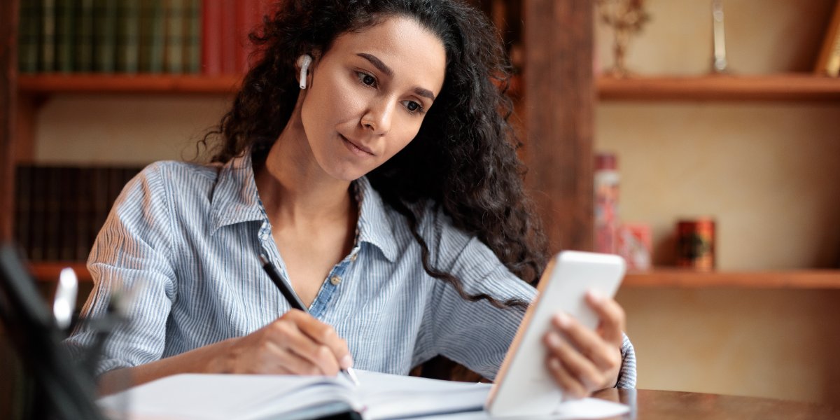 mobile learning, femeie care urmareste un curs online pe mobile si ia notite